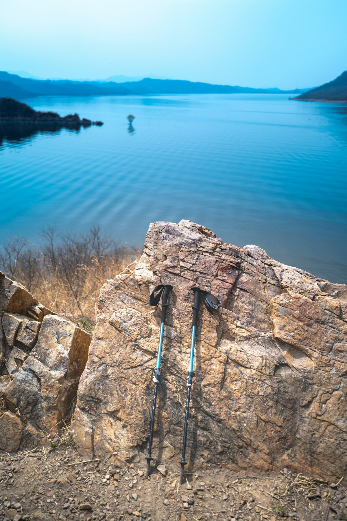 Trekkingstöcke lehnen an einem Felsen mit Blick auf einen See